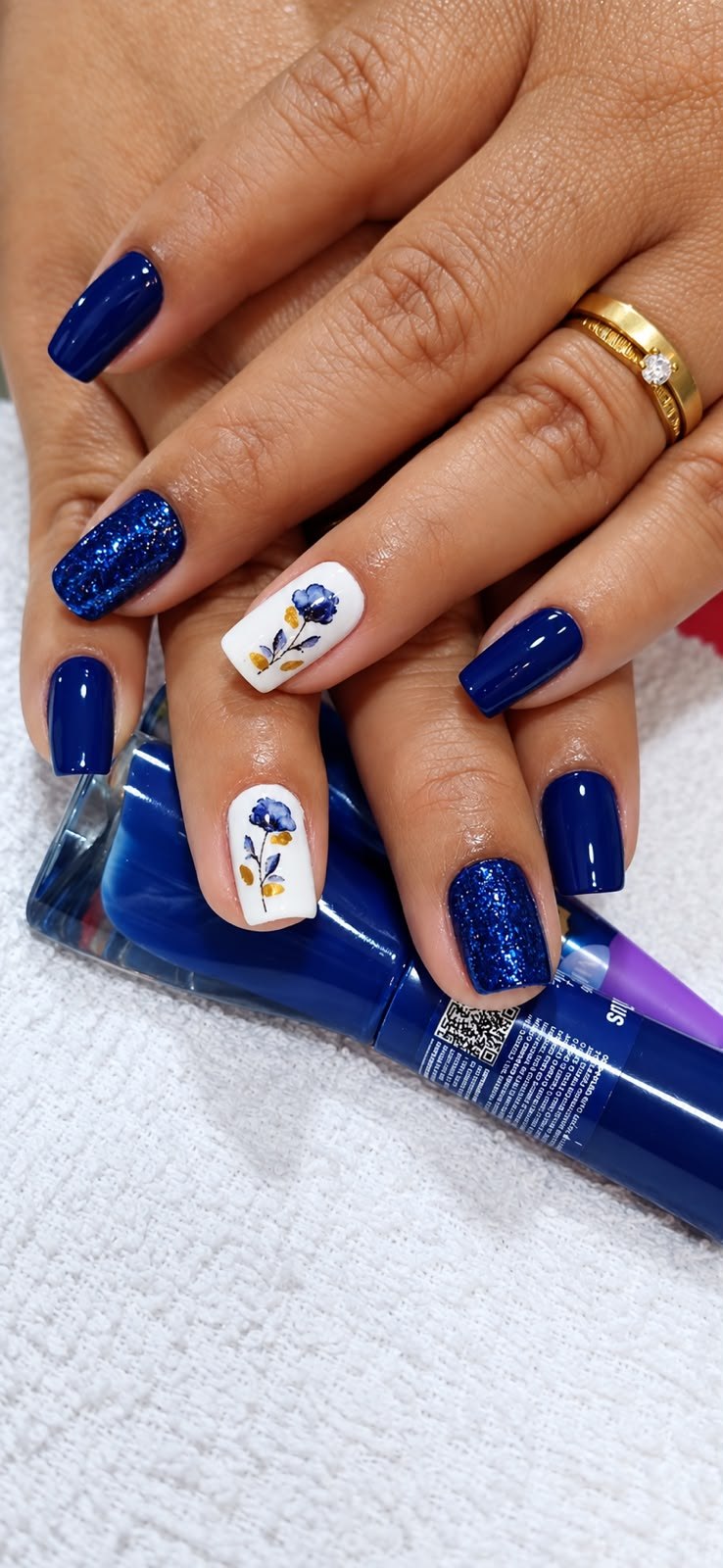 Unhas azul marinho com glitter e duas unhas brancas decoradas à mão com flores, feitas no Espaço Glamour da Su